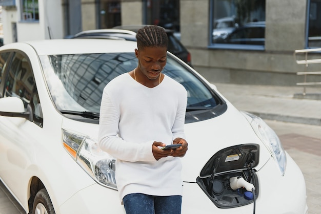 L'uomo africano usa lo smartphone durante l'attesa e l'alimentazione si collega ai veicoli elettrici per caricare la batteria in auto
