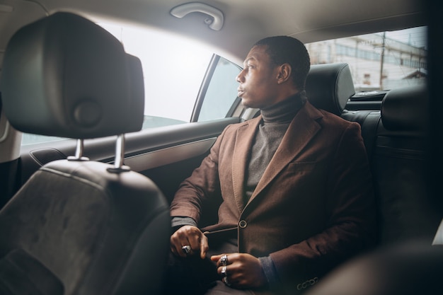 アフリカの男が車の後部座席に座っている間スマートフォンを使用しています。