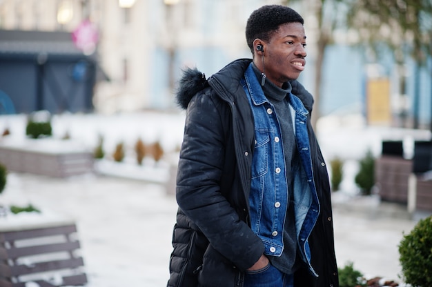 African man wear on jacket at cold winter weather posed outdoor with headphones on ears.