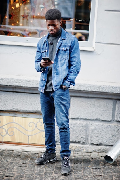 African man wear on jeans jacket posed outdoor with cell phone at hand