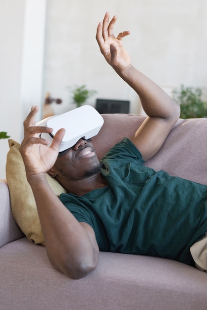 African man wearing vr glasses lying on sofa and gesturing during game