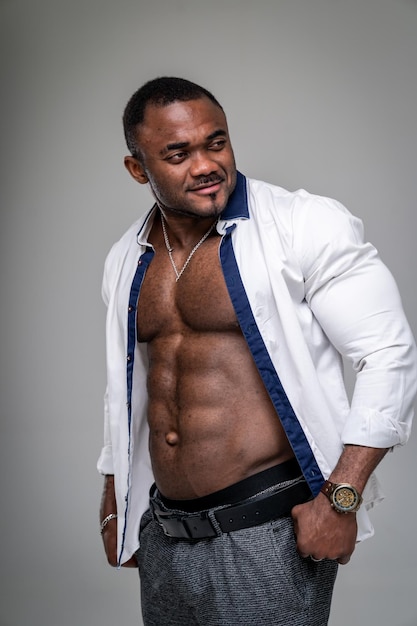 African man wearing white shirt and grey trousers standing halfturned Muscular man in white unbuttoned shirt Smiling guy with stong naked abs