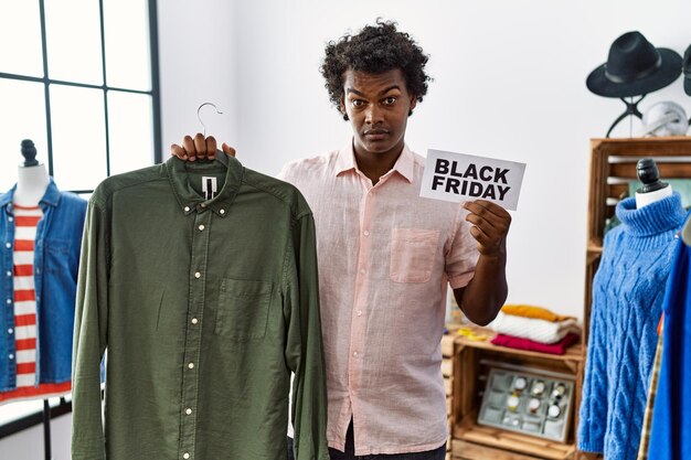 African man with curly hair holding black friday banner at retail shop clueless and confused expression. doubt concept.