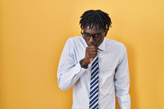 African man with dreadlocks standing over yellow background feeling unwell and coughing as symptom for cold or bronchitis. health care concept.