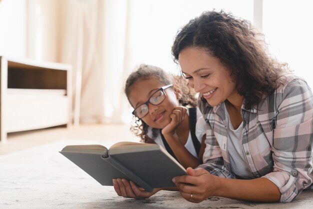 African mother mom reading fairy tales book novel with daughter girl learning together helping assisting with homework for school Homeschooling with nanny