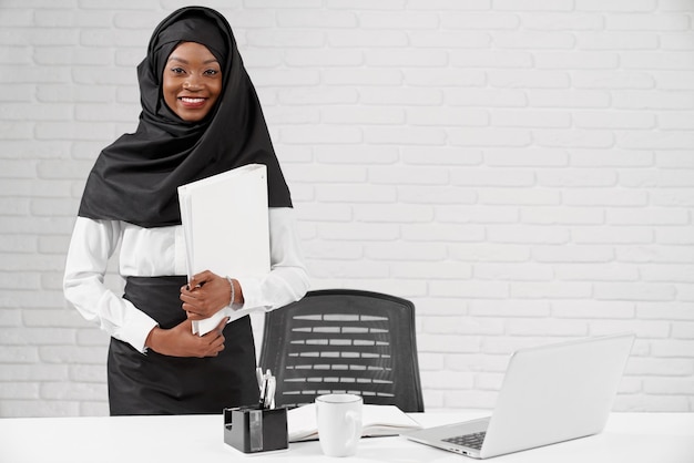 African muslim woman standing at table holding folder
