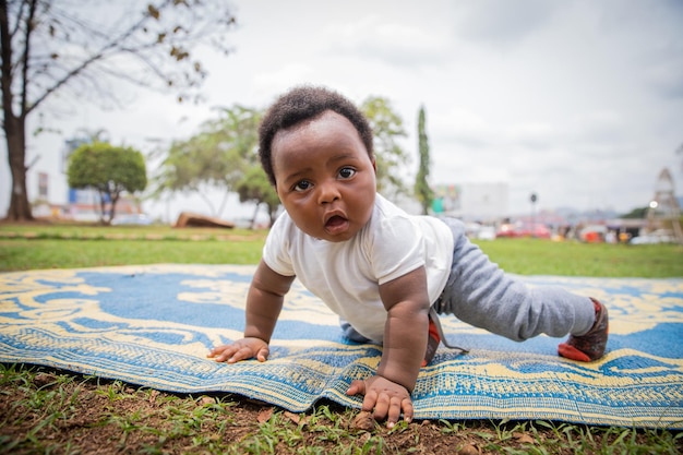 An African newborn with a surprised look crawls on a picnic tablecloth