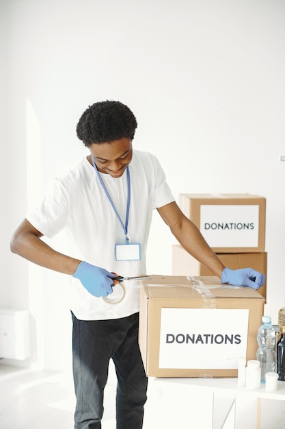 African in protective gloves. Guy packs a box. Volunteer with humanitarian aid.