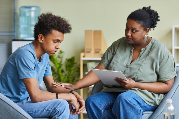 Photo african psychologist supporting depressed teenage boy feeling guilty about behavior during therapy a