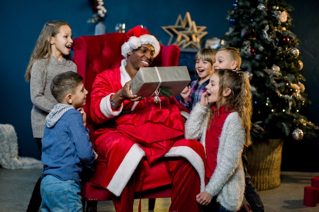 African Santa Claus sitting in armchair and giving the presents to little children