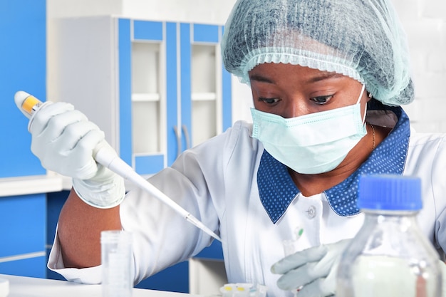 African scientist, technical assistant in lab coat, protective hat and gloves optimizes PCR testing for SARS-CoV-2 virus in modern test laboratory