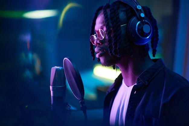 African singer with dreadlocks singing to microphone and recording a song the recording studio