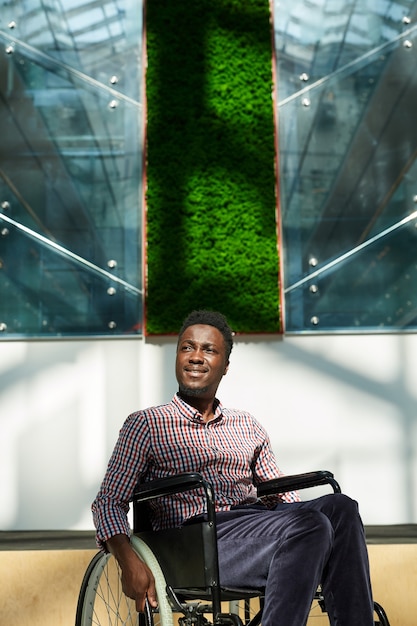 彼はオフィスで働いている車椅子に座っているアフリカの笑顔の実業家