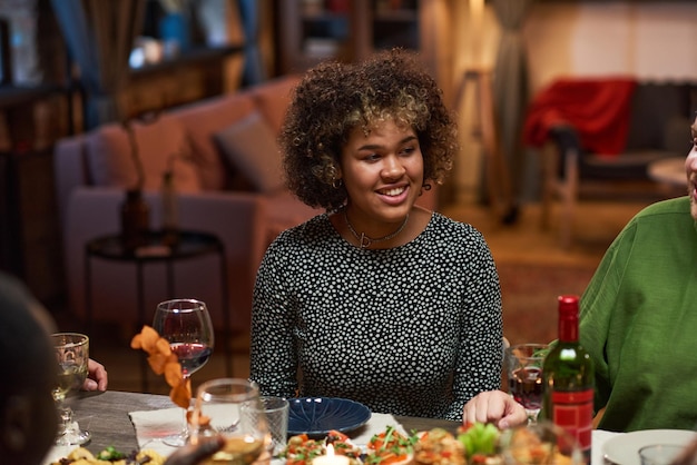 African smiling woman sitting at dining table during a dinner party in the living room