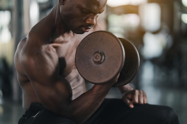 African sport man strong muscle working out excercise in\
weights with dumbbell at fitness room at the gym body building\
sport man fitness concept