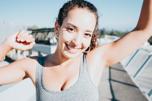 African sports woman standing celebrating finishing exercise smiling to camera urban sport scenario. Sunset time. Beauty healthy arab woman. Sport cloths, new habits for a new year, lose weight.