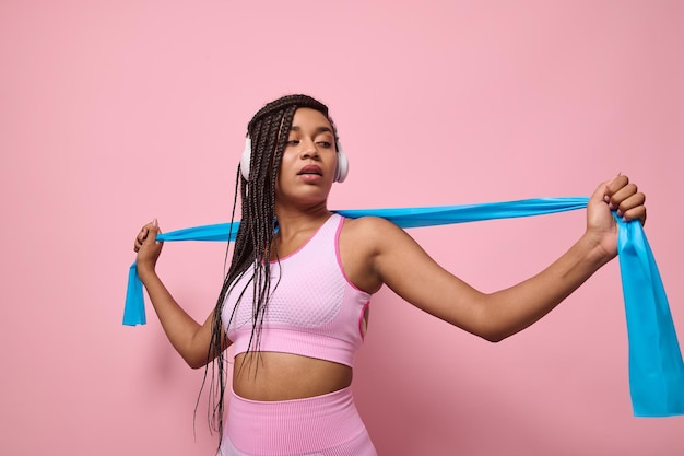 Photo african sportswoman performs exercises with resistance band. people, sport and fitness. young woman training with elastic strap on pink background. active lifestyle concept