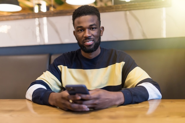 Фото Африканский студент с помощью мобильного телефона смотрит на экран с серьезным и сосредоточенным выражением лица за чашкой кофе в кафе