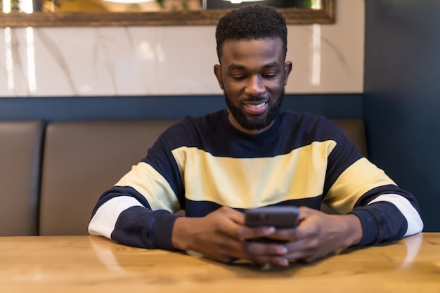 African student   using mobile phone, looking at the screen with serious and concentrated expression while having coffee at a cafe