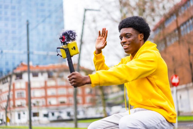 Photo african stylish vlogger recording video and waving in the city