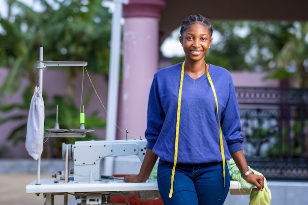 African tailor happily standing in front of her sewing machine