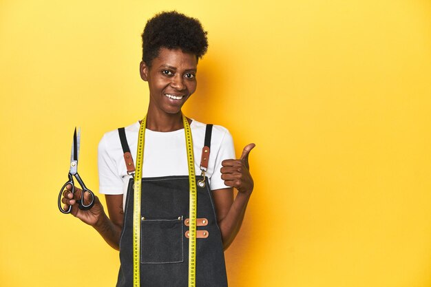 African tailor with scissors and measuring tape fashion concept smiling and raising thumb up