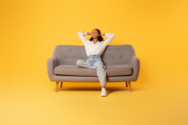 African teen girl relaxing sitting on sofa over yellow background