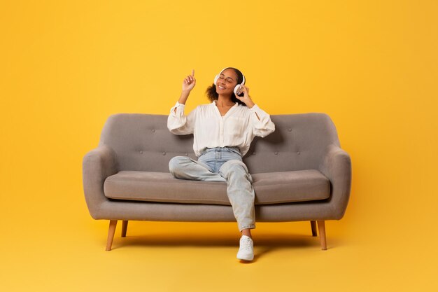 African teen girl relaxing with headphones on couch yellow backdrop