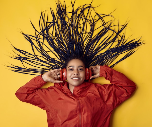 African teenage girl with dreadlocks in red windbreaker listening music