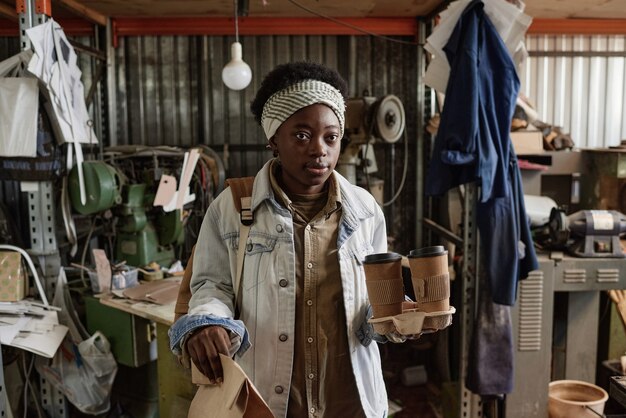 African woman carrying coffee cups and packet with breakfast\
while coming to work in the morning