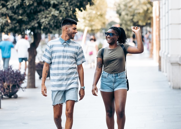 African woman gesticulating happily while talking to a young caucasian man walking in a city. Spain