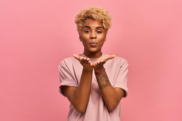 African woman has a blonde haircut, stretches hands near face, blows air kiss