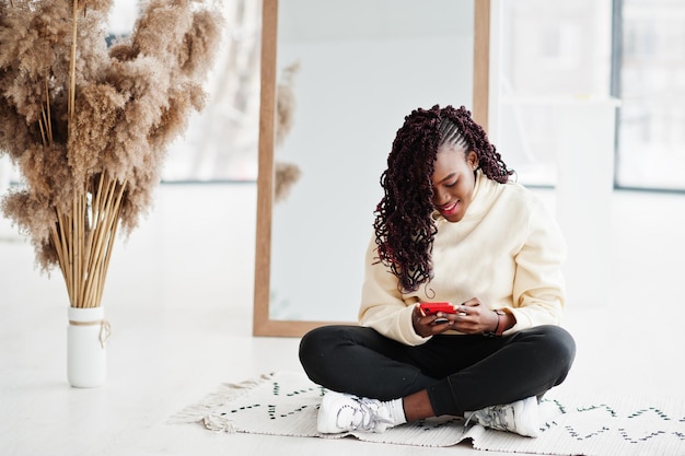 パーカーを着たアフリカの女性が携帯電話で屋内の鏡の近くでポーズをとる。