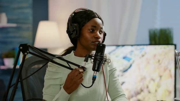 African woman host of online show talking into microphone wearing headphones. Speaking during livestreaming, blogger discussing in podcast wearing headphones, on-air production internet broadcast