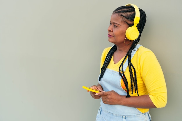 African woman listening to music and using a smartphone while standing on a gray background.