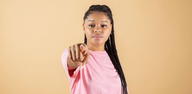 African woman pointing finger at camera, serious face, yellow background