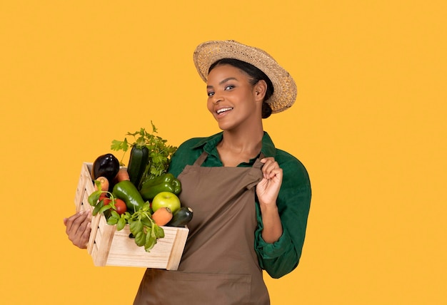 黄色い背景の箱の中の野菜とポーズをとるアフリカの女性