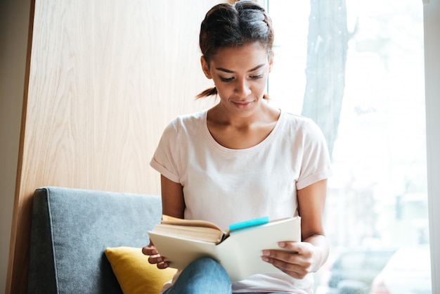 African woman reading book near the window