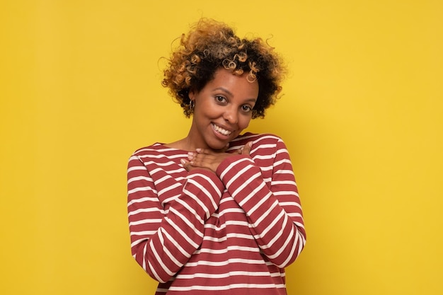 African woman smiling broadly and keeping hand on her chest glad to receive compliment