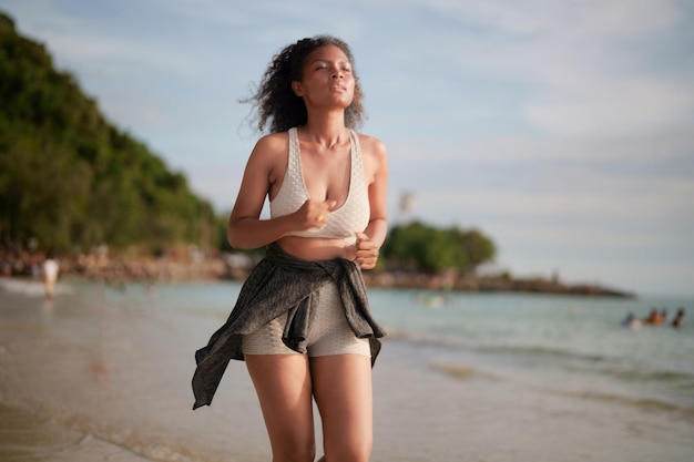 African woman in sport bra is running on beach for outdoor workout Portrait sexy Asian African lady preparing herself for fitness at beach