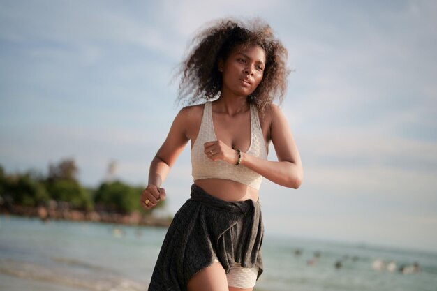 African woman in sport bra is running on beach for outdoor workout Portrait sexy Asian African lady preparing herself for fitness at beach