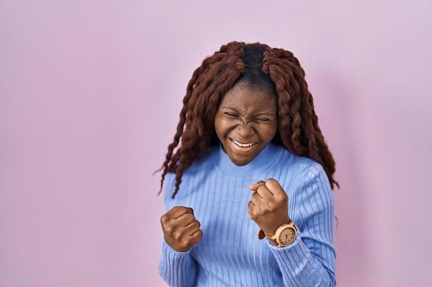 African woman standing over pink background very happy and excited doing winner gesture with arms raised smiling and screaming for success celebration concept