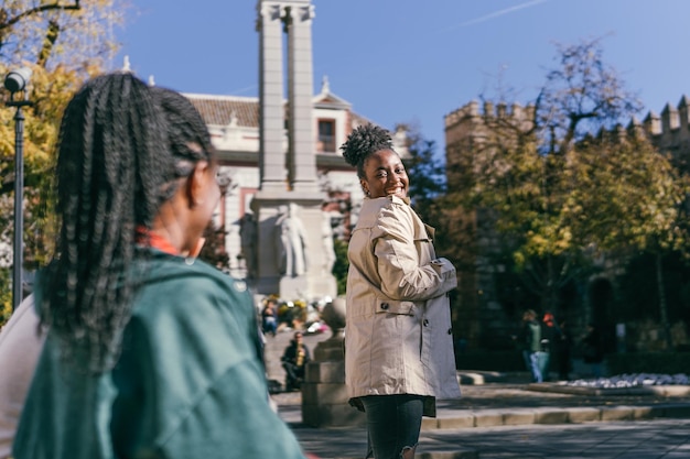 African woman trying on the trench coat she has just received as a gift in a square next to a friend