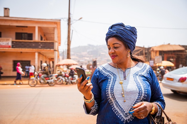 Una donna africana usa il suo smartphone mentre si trova nel centro della città e indossa abiti tradizionali africani