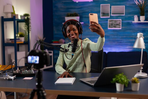 African woman using smartphone to take photo in entertainment business recording episode. On-air online production internet podcast show host streaming live content, recording digital social media.