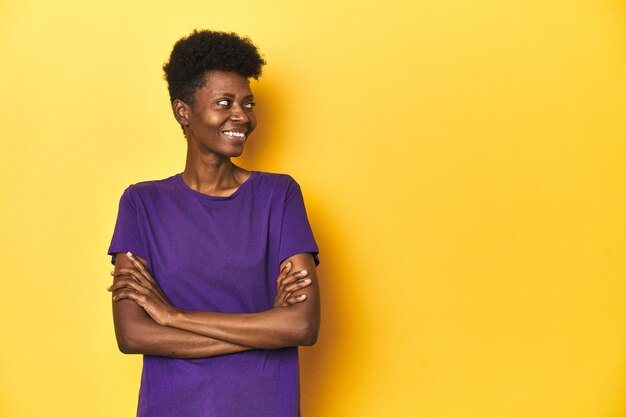 African woman in violet tee yellow studio scene smiling confident with crossed arms