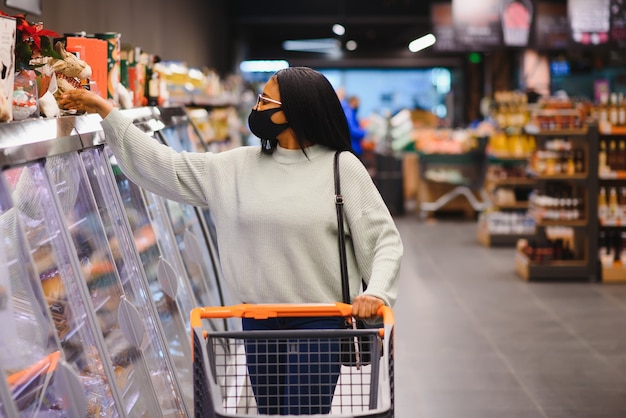 일회용 의료 마스크를 착용하는 아프리카 여자. 코로나 바이러스 전염병 발생시 슈퍼마켓에서 쇼핑. 전염병 시간.