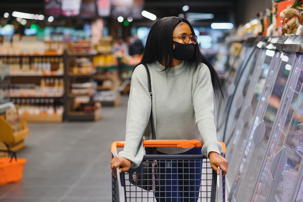 African woman wearing disposable medical mask. Shopping in supermarket during coronavirus pandemia outbreak. Epidemic time.