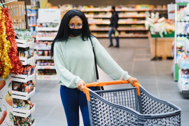 African woman wearing disposable medical mask. shopping in\
supermarket during coronavirus pandemia outbreak. epidemic\
time.