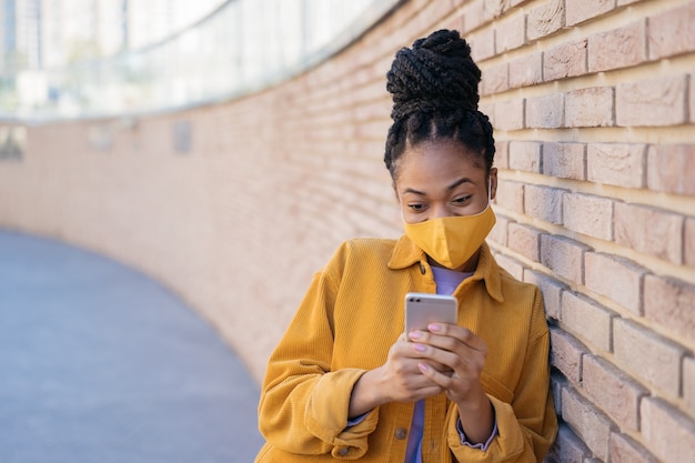 African woman wearing protective face mask using mobile phone text messaging shopping online